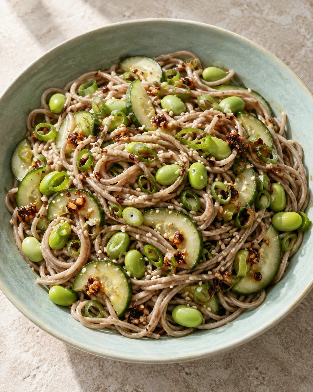 Cold soba noodles with cucumber half-moons, green edamame, scallions, sesame seeds, and original chili crisp