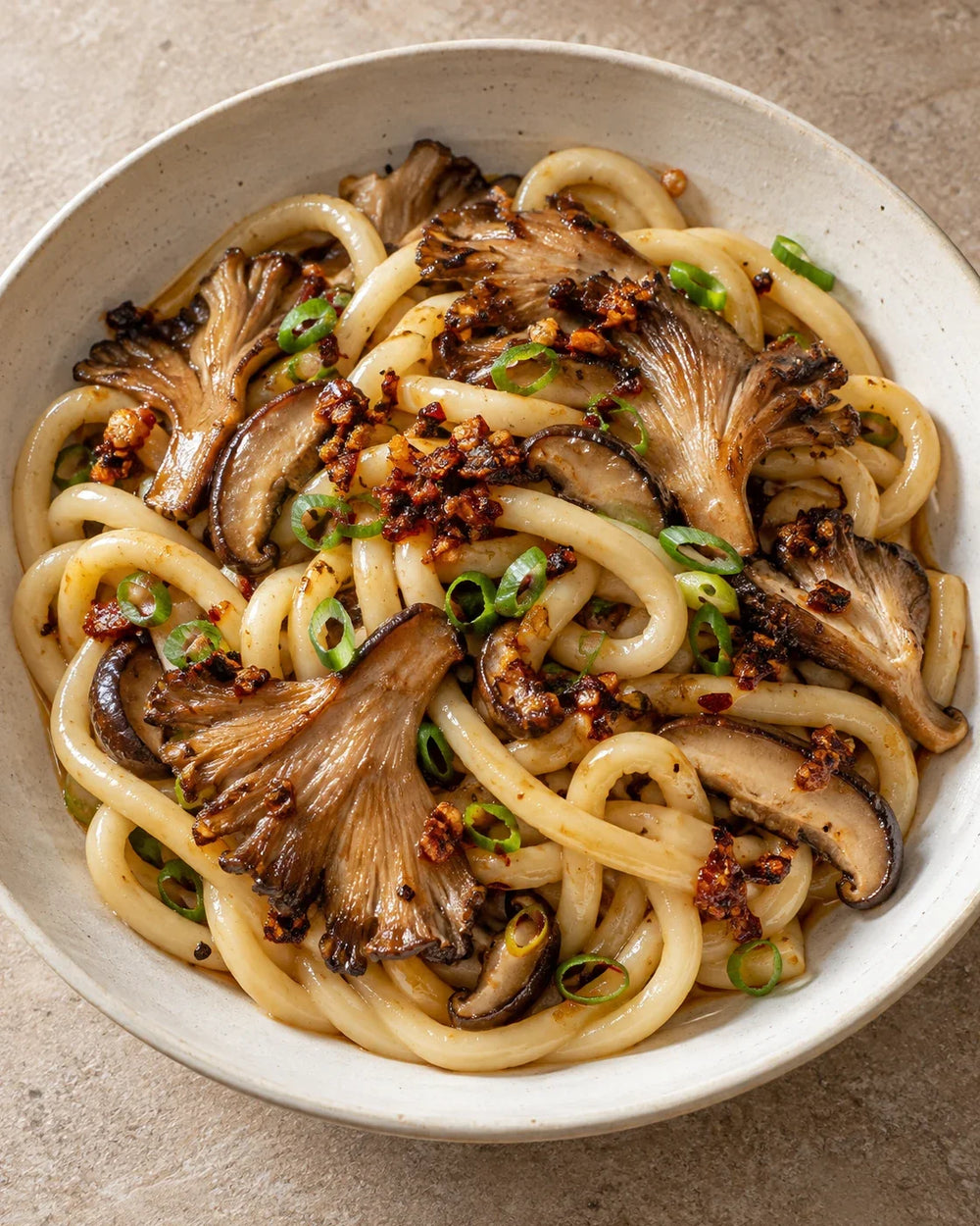 Thick udon with browned oyster and shiitake mushrooms, scallions, and visible garlic-shallot chili crisp